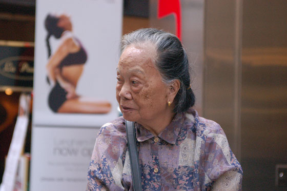 MID LEVELS - Il volto di un'anziana cinese contrasta con l'immagine dell'eterna giovinezza della pubblicità sullo sfondo