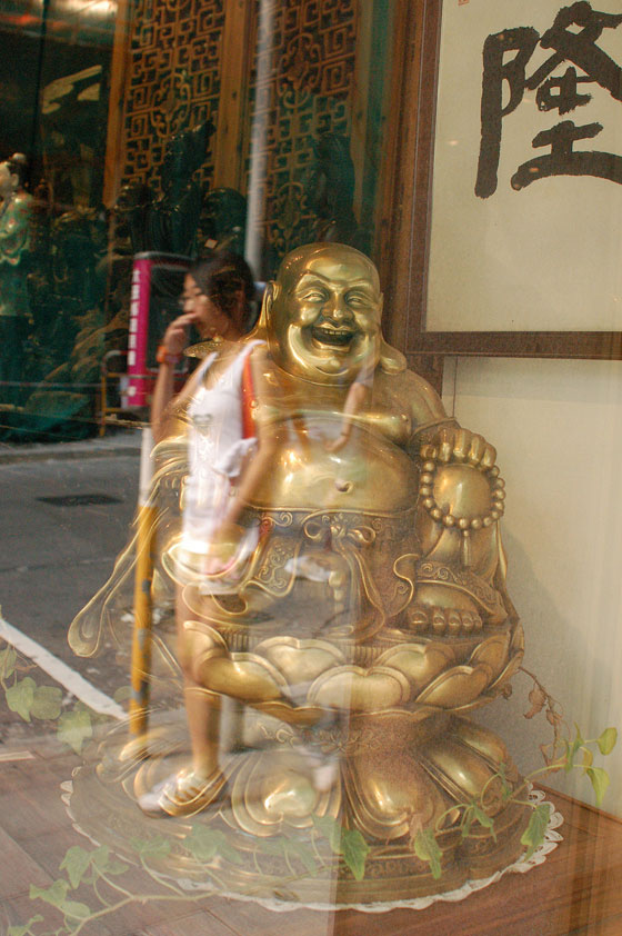 HOLLYWOOD ROAD - L'immagine di una passante riflessa nella vetrina che espone il Buddha felice Maitreya