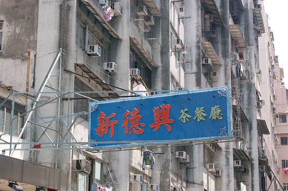 WAN CHAI - In primo piano una grande insegna con ideogrammi cinesi e sullo sfondo vecchi condomini con le facciate annerite