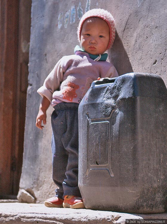 LEH  - Città vecchia: un piccolo bambino tibetano fuori dalla porta di casa si appoggia ad una tanica timidamente incuriosito dalla nostra presenza