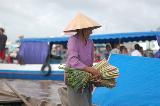 DELTA DEL MEKONG - Cai Rang: una indaffarata nonnina porge un mazzo di ortaggi ad una barca vicina, probabilmente della sua stessa famiglia