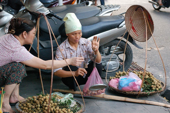 HANOI - Una venditrice ambulante pesa la frutta con una vecchia stadera