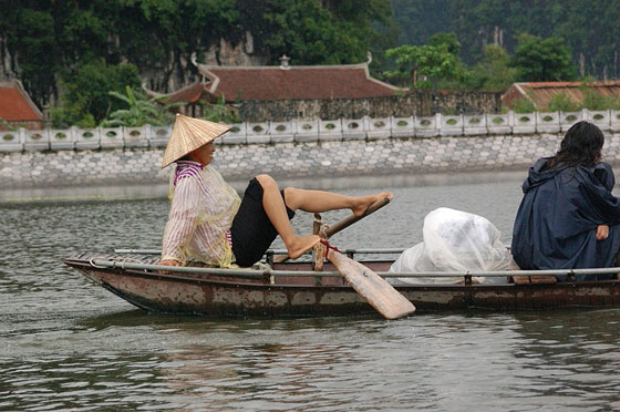TAM COC - La barcaiola che rema con i piedi sullo sfondo di un caratteristico padiglione o tempio vietnamita