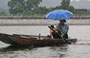 TAM COC. Un vietnamita rema con i piedi, tiene in mano l'ombrello e fuma la sigaretta con assoluta disinvoltura